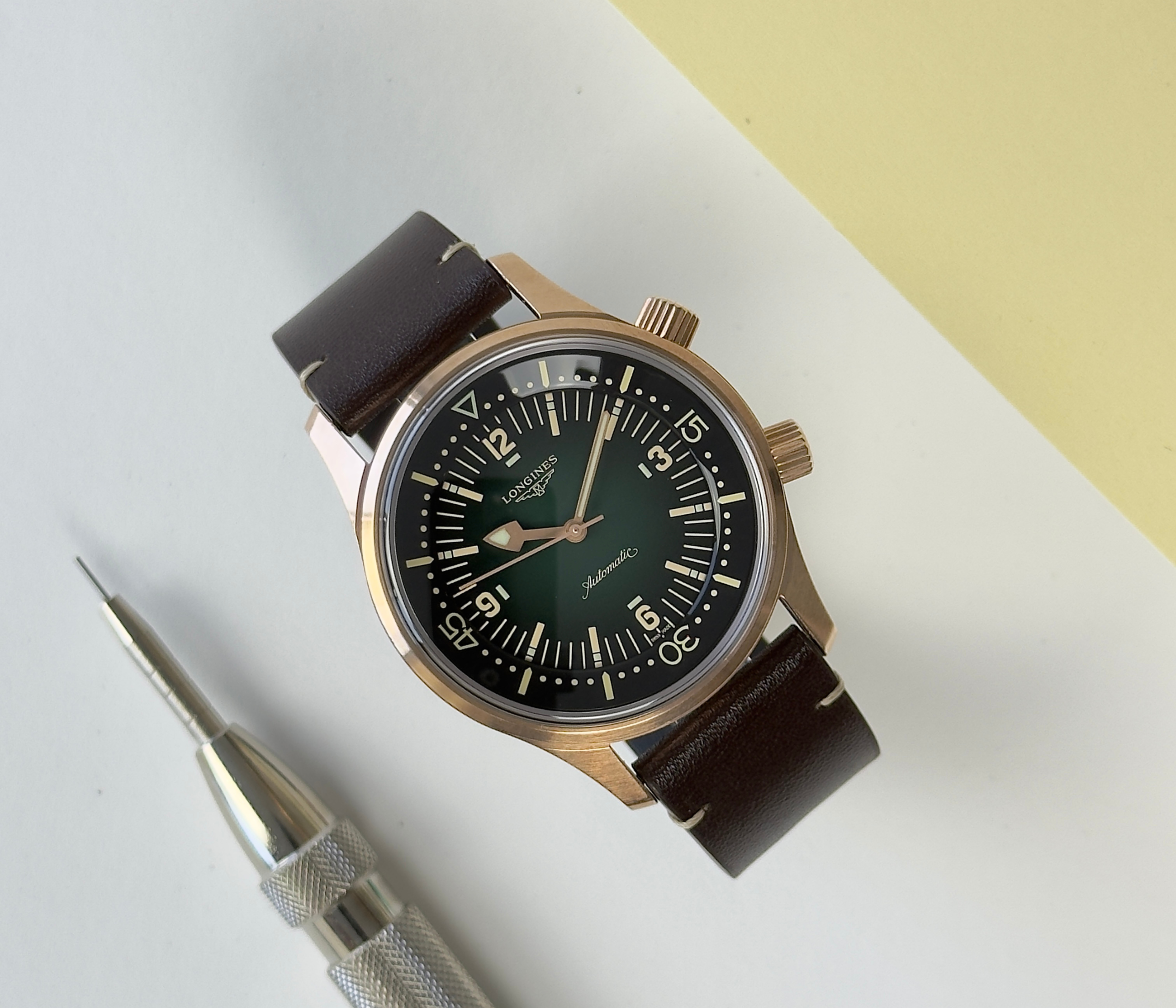 Longines Legend Diver L37741502 (2023) i bronze med grøn skive på en brun læderrem. Uret fremstår i god stand med et tryk på den ene side af kassen. Kommer som fuldt sæt: Bokse, certifikat, manualer, lænkeværktøj samt tre ekstra remme.