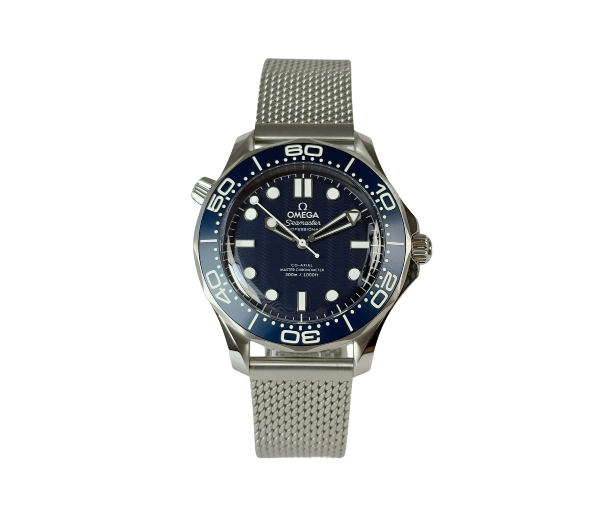 Omega Seamaster Diver 300M James Bond 60th Anniversary 210.30.42.20.03.002 (2026) i stål med blå oxideret aluminiumsurskive med lasergraverede bølger. Uret måler 42 mm og er udstyret med en flot mesh-lænke. Uret fremstår i mint stand uden brugsspor og er delvist i fabriksfolie, 10/10. 
Kommer som fuldt sæt: Bokse, certifikater, manual mv. 
Uret er solgt fra forhandler i Cannes i marts 2026.