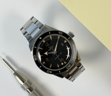 Omega Seamaster 300 Heritage 234.30.41.21.01.001 (2022) i stål med sort skive og sort oxideret aluminiumskrans med vintage Super-LumiNova. Uret fremstår i god alm. stand, 8/10. Kommer som fuldt sæt: Bokse, certifikater, manualer mv. 
