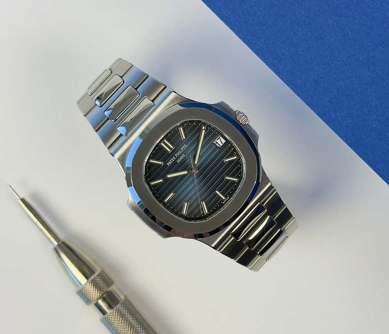 Patek Philippe Nautilus 5711/1A (2014) i stål med blå skive og integreret lænke. Uret måler 40 mm med en tykkelse på 8.6 mm, hvilket giver uret en elegant lav profil på håndleddet.
Uret fremstår i utroligt flot og upoleret stand med mindre brugsspor, +9/10.
Kommer som fuldt sæt: Bokse, certifikat, manualer, lædermappe mv. 