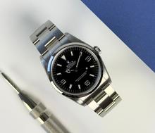 Rolex Explorer 114270 (2008) i stål med ROLEX i rehaut. Uret måler 36 mm, er vandtæt til 100 meter og i nær ny stand uden brugsspor, 9.5/10. Kommer som fuldt sæt: Bokse, certifikat, manualer, hangtag,whitetag og 2026 Rolex-service med servicestickers