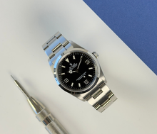 Rolex Explorer I 114270 (2002) i stål på Oysterlænke med sort Explorer-skive. Uret fremstår i rigtig flot stand, 8.5/10. Kommer med originalt certifikat, grønt hangtag samt et ekstra led. 
Y-serie (Y86XXXX) fra 01/02 solgt i 2003. 