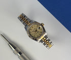 Rolex Datejust 79173 (2002) i guld og stål. Dette klassiske dame Datejust i 26 mm har en champagne Tapestry skive, jubileelænke og safirglas. Lænke uden stræk. Uret fremstår i rigtig flot stand, 9/10. Et utrolig flot og feminint ur, der er den perfekte kombination af ur og smykke. 
